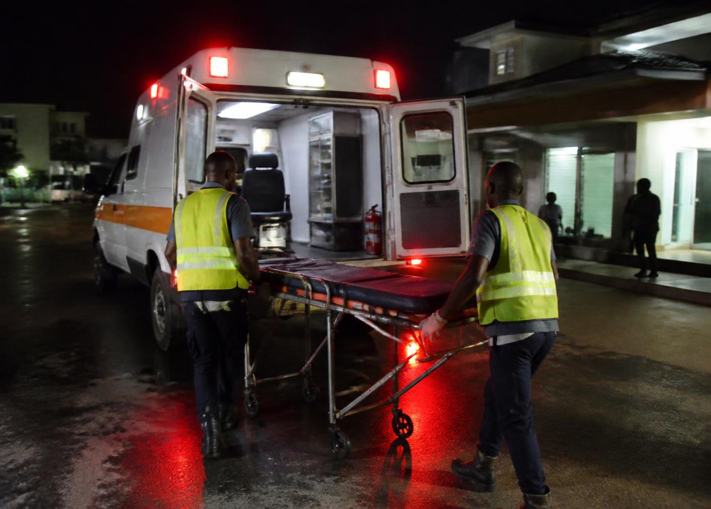 Paramedics wheeling a stretcher to an ambulance outside a Kampala clinic at night
